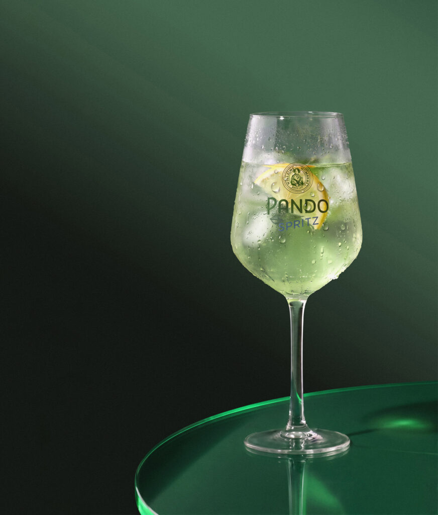 Copa de Pando Spritz con hielo sobre fondo verde oscuro